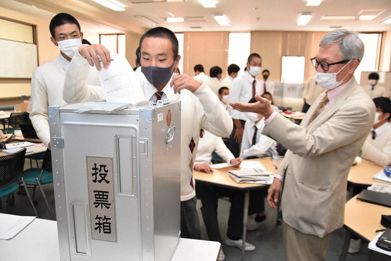 A young Japanese man placing his vote in a ballot box.
