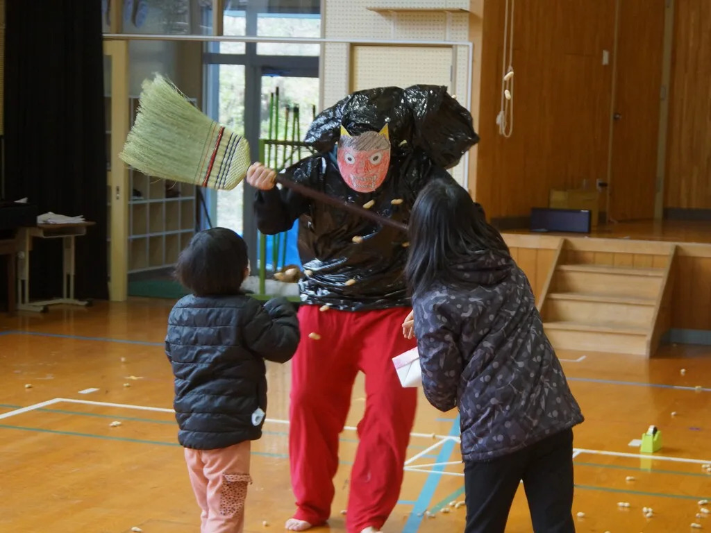 A person dressed as an oni has beans thrown at them by children.