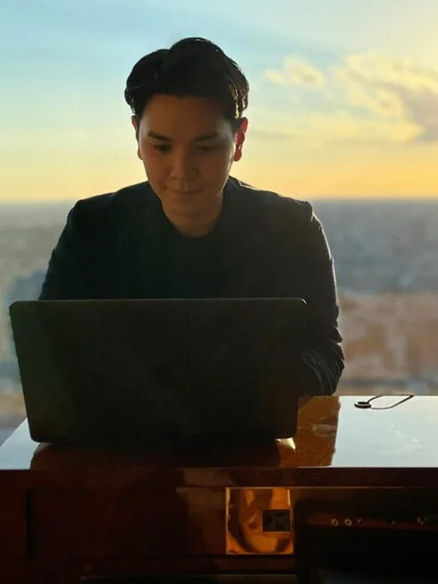 Arashiro Yasuta - a Japanese lawyer specialising in Japanese cbd law. He is looking at a laptop, with a far-away city skyline behind him at sunset.